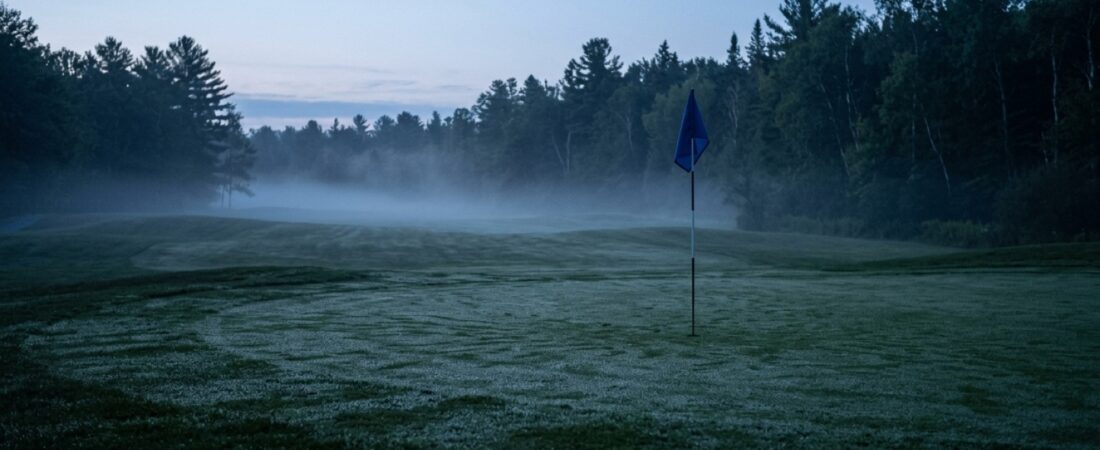 Tyhjä golfkenttä hämärässä, sumua väylällä ja lipputanko kaukaisella viheriöllä sinisessä valossa
